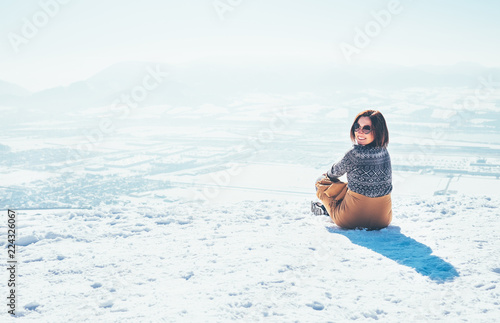 Happy smiling woman sits on the snowy mountain hill over the city. Sunny winter beautiful weather day © Soloviova Liudmyla
