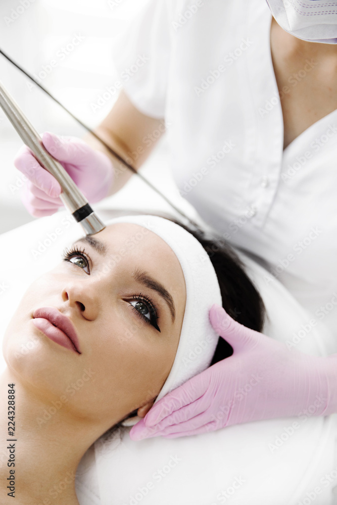 A woman came to laser hair removal facial. The woman lies and smiles, the doctor leads him in the face with a modern laser epilator. They are in the modern clinic.close up A woman came to laser hair removal facial. The woman lies and smiles, the doctor leads him in the face with a modern laser epilator. They are in the modern clinic.close up