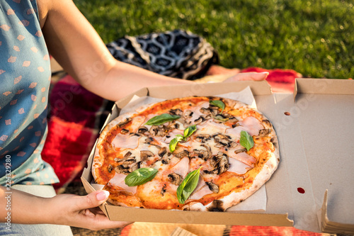 Happy young woman holding hot pizza in box, seat outdoor in street