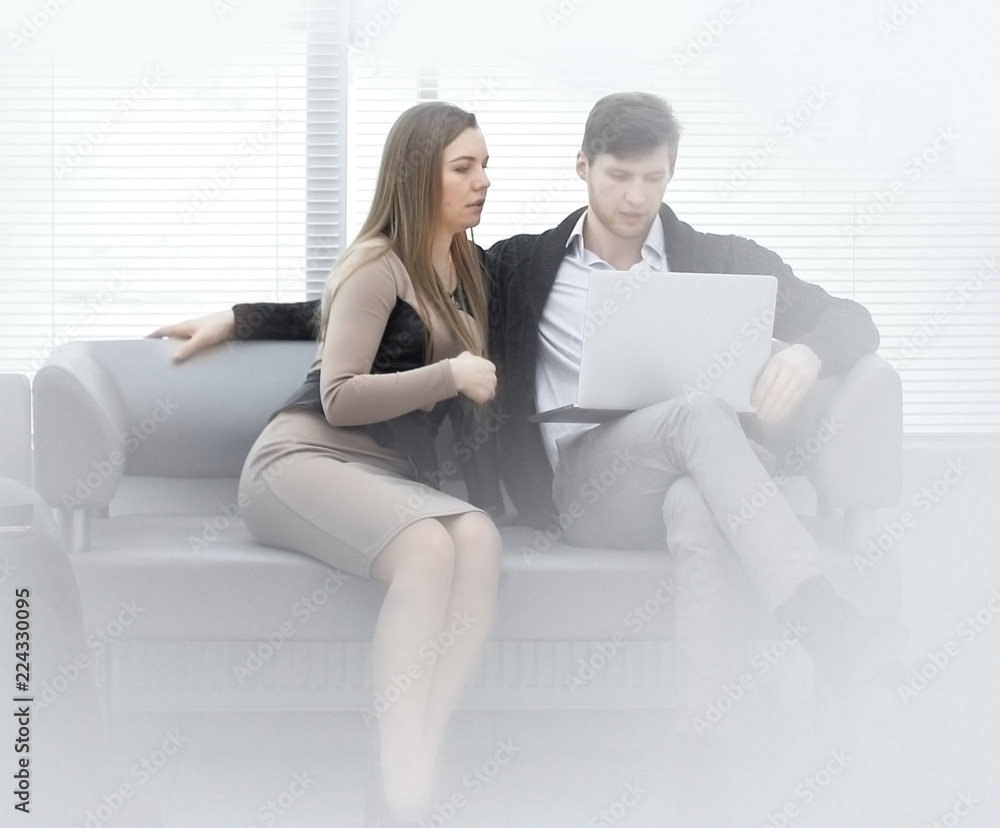 two employees of the company work on a laptop, sitting near a window in the office two employees of the company work on a laptop, sitting near a window in the office