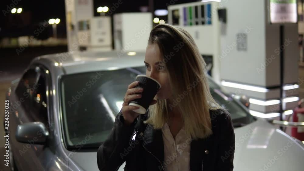Having rest. Pretty smiling woman leaning on the car and holding black paper cup, drinking coffee. Front view Having rest. Pretty smiling woman leaning on the car and holding black paper cup, drinking coffee. Front view