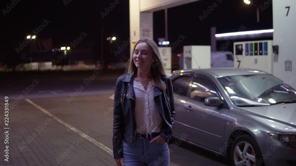 Portrait of romantic, smiling woman at the gas station in caual, the car in the background walks and posing. Front view. Night time Portrait of romantic, smiling woman at the gas station in caual, the car in the background walks and posing. Front view. Night time