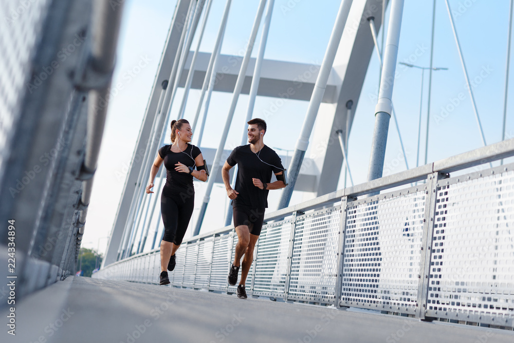 Young couple doing morning workout outdoors. Young man and woman running on bridge. Young couple doing morning workout outdoors. Young man and woman running on bridge.