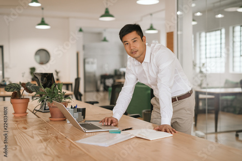 Young Asian businessman leaning on his desk using a laptop photo