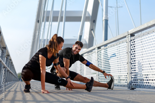 Young couple doing morning workout outdoors. Young man and woman stretching they muscle before running on bridge.