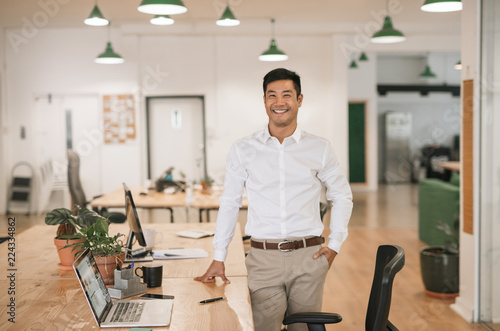 Smiling Asian businessman standing by his desk in an office