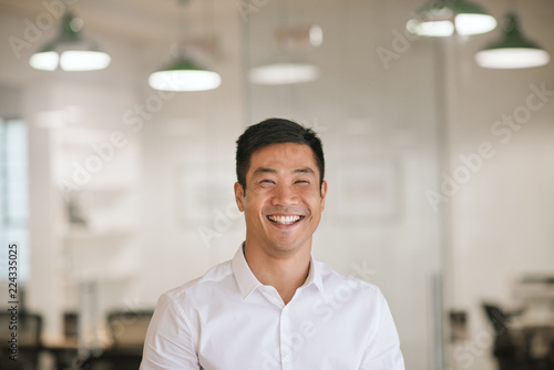 Young Asian businessman laughing while standing in a modern office