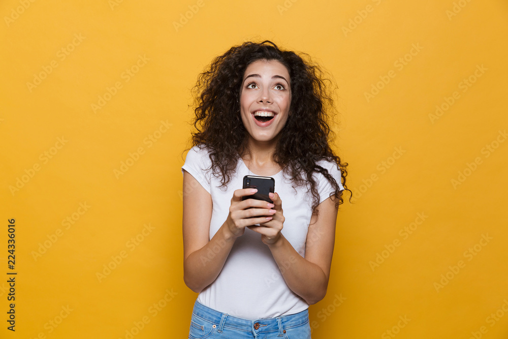 Happy cute young woman posing isolated over yellow background using mobile phone. Happy cute young woman posing isolated over yellow background using mobile phone.