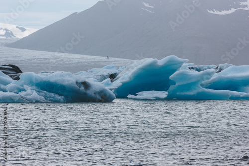 glacier ice pieces floating in lake in Iceland with mountain silhouette on background