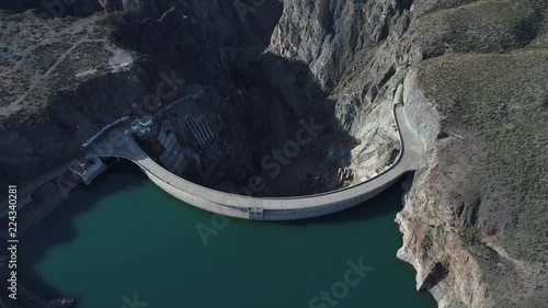 Aerial drone scene of Agua de Toro Dam. Flying over semi circular concrete dam structure camera panning to senital view. Mountains and river canyon at background. San Rafael, Mendoza, Argentina photo