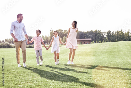 Family walk. Family of four walking on grassy field looking at e