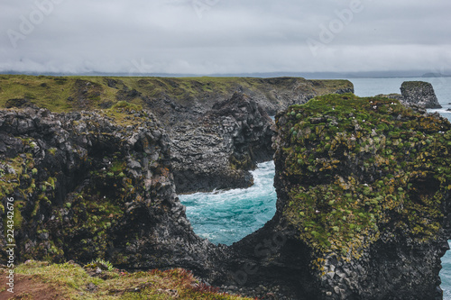 beautiful mossy cliffs in front of blue ocean in Arnarstapi, Iceland on cloudy day