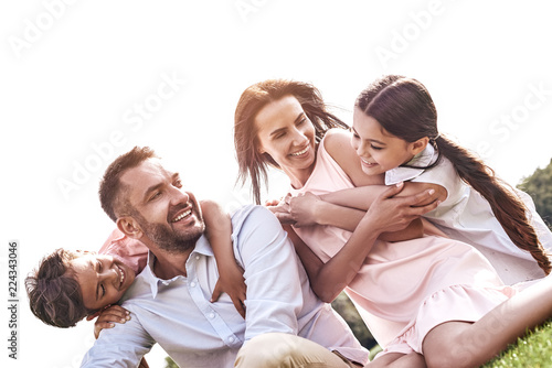 Bonding. Family of four sitting on a grassy field hugging smilin