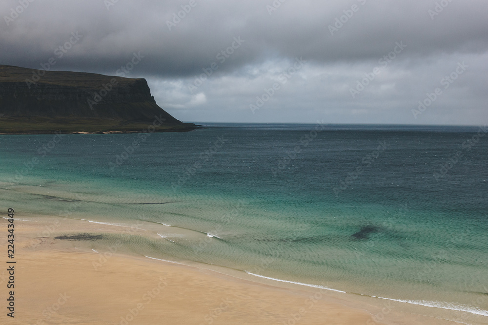 Dramatic shot of sandy beach and blue ocean with cliff in Iceland under stormy sky