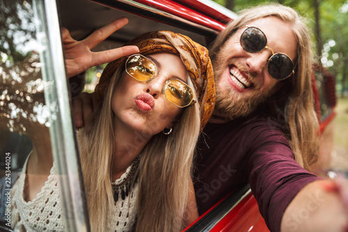Bild auf Leinwand Photo of kind hippie couple smiling, and showing peace sign while driving retro