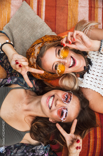 Konstfotografi Photo from top of two joyful hippie girls, smiling and lying on blanket outdoor