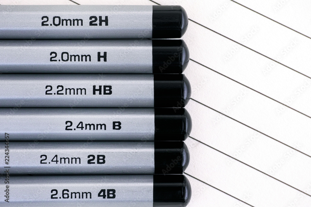 Gray graphite pencils with graphite grading scale in a row on lined paper.  Stock Photo | Adobe Stock