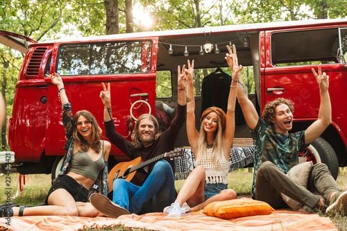 Fototapeta Group of friends hippies men and women rejoicing, and sitting near vintage miniv