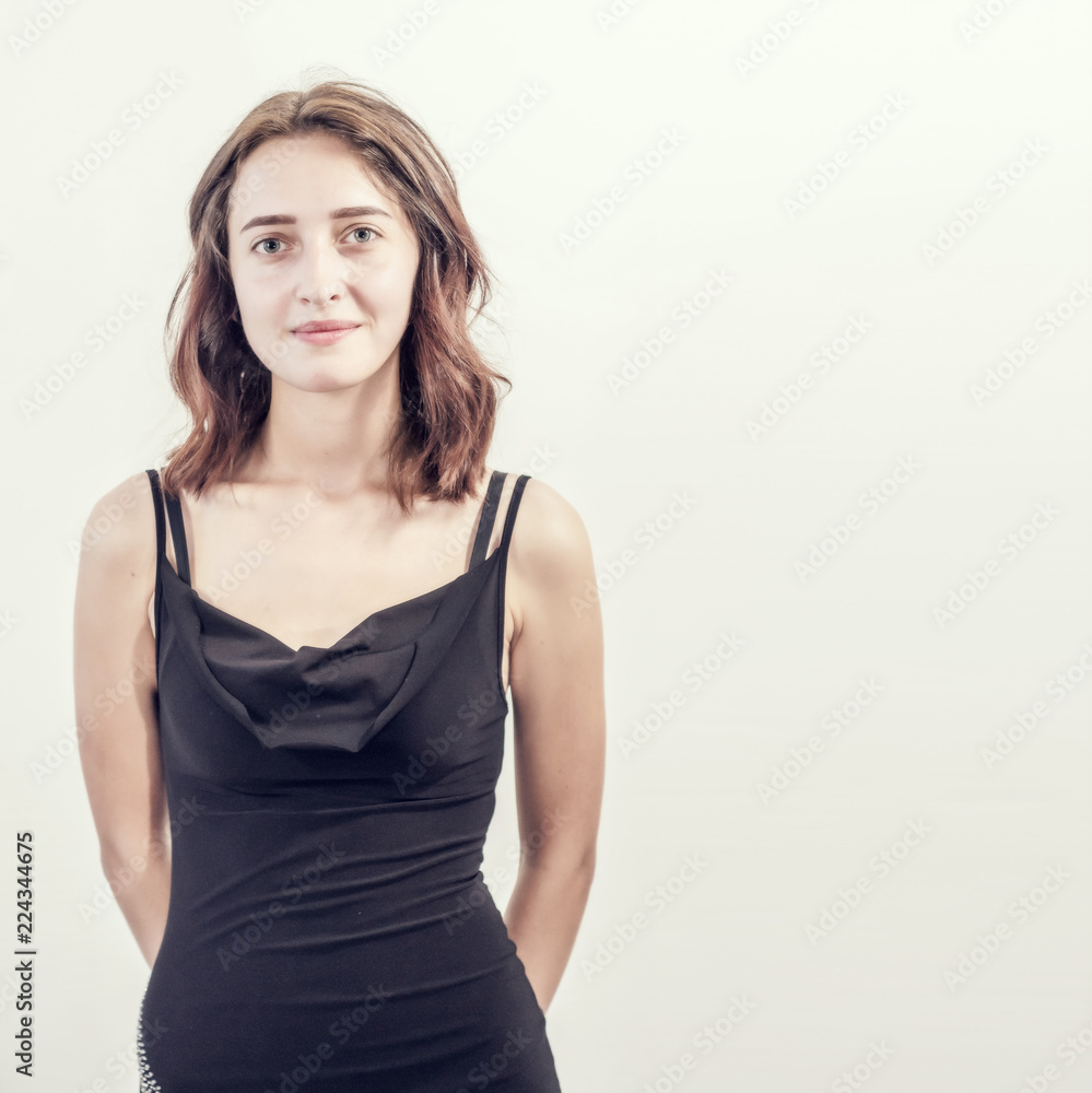 Beautiful young girl in short black dress is standing on white background, smile, beautiful face, brunette. Beautiful young girl in short black dress is standing on white background, smile, beautiful face, brunette.