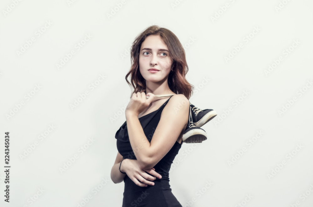 beautiful young girl in a short black dress holds sneakers behind her shoulders on laces beautiful young girl in a short black dress holds sneakers behind her shoulders on laces