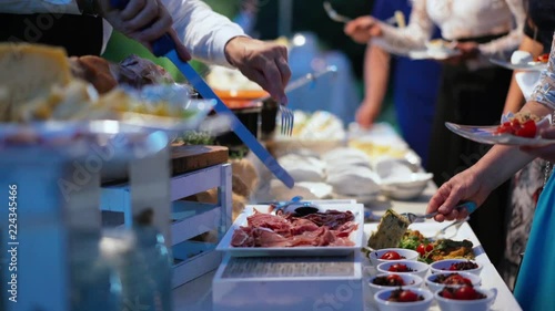 People choosing food during on the buffet table in the catering party outdoor ay night time. Table with food and hands of people.