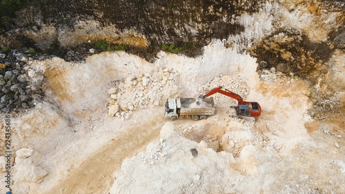 Excavator loads the truck in a limestone quarry. Aerial view wheel loader excavator machine loading dumper truck at quarry. Earth mover loading dumper truck with rocks in quarry. Philippines. Travel