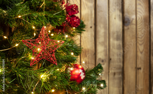 Christmas toy red star on a Christmas tree with a garland next to red balls on a wooden background