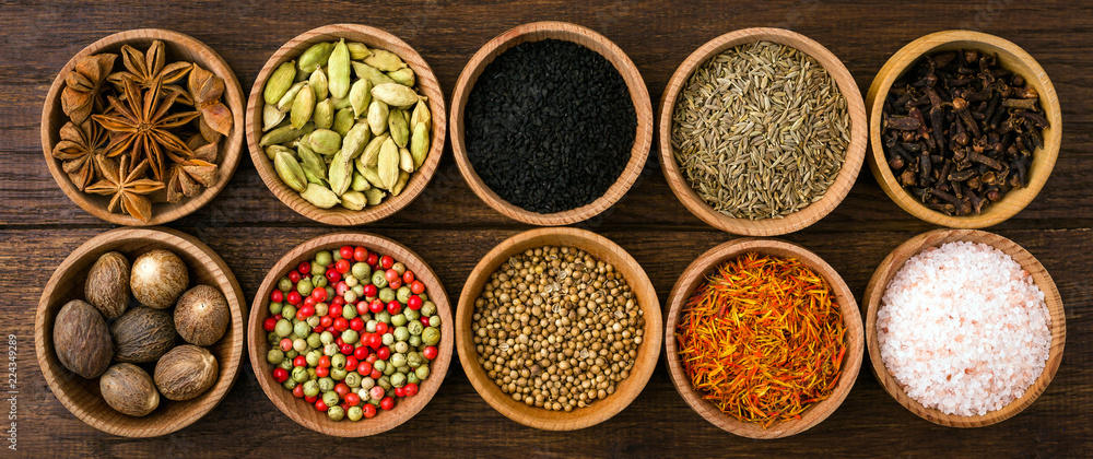 Spices on a wooden background in bowls, place of copying, seasoning, saffron, cumin, black sesame, cardamom, nutmeg, pink salt, star anise, coriander, long banner