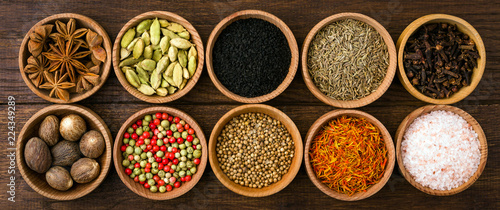 Spices on a wooden background in bowls, place of copying, seasoning, saffron, cumin, black sesame, cardamom, nutmeg, pink salt, star anise, coriander, long banner