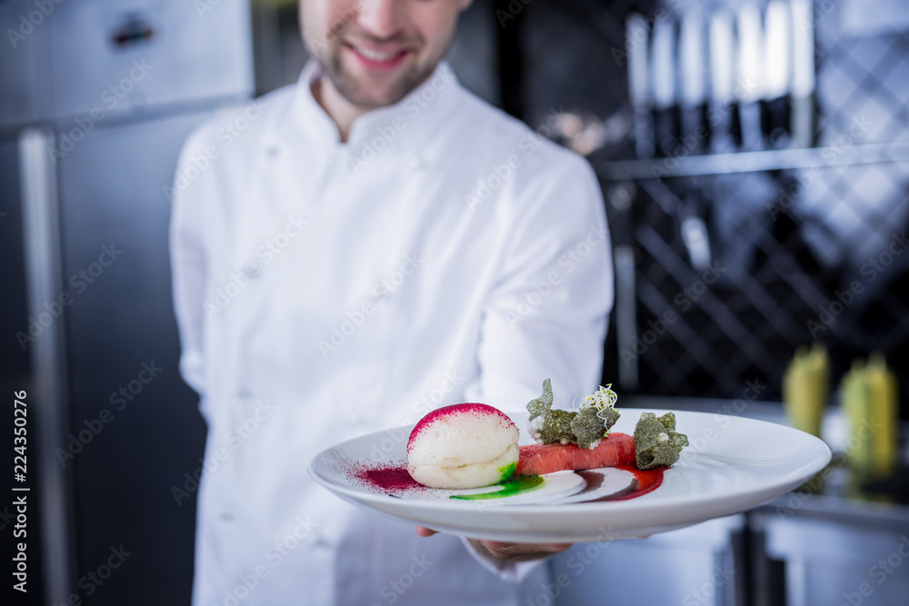 Bon appetit. Happy pleasant cook feeling good while holding a plate with a dessert Bon appetit. Happy pleasant cook feeling good while holding a plate with a dessert