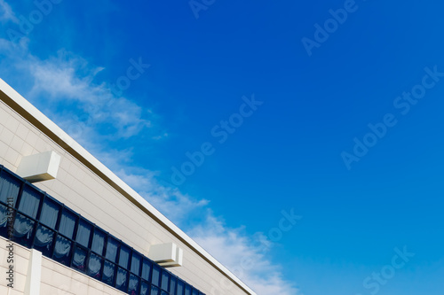 The abstract blue background with the sky and the white wall of the modern building with the row of windows. Empty space for your design.