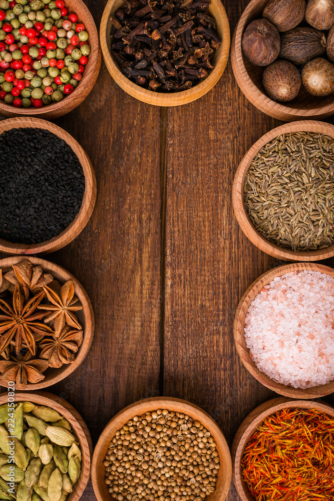 Spices on a wooden background in bowls, frame, place of copying, seasoning, saffron, cumin, black sesame, cardamom, nutmeg, pink salt, star anise, coriander