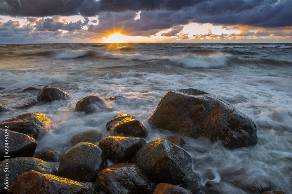 Obraz premium A sea landscape with rocks, a storm and a setting sun. Waves, rocks, storm and clouds. 