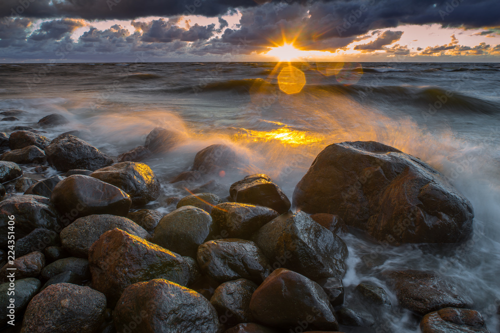 Obraz premium A sea landscape with rocks, a storm and a setting sun. Waves, rocks, storm and clouds. 