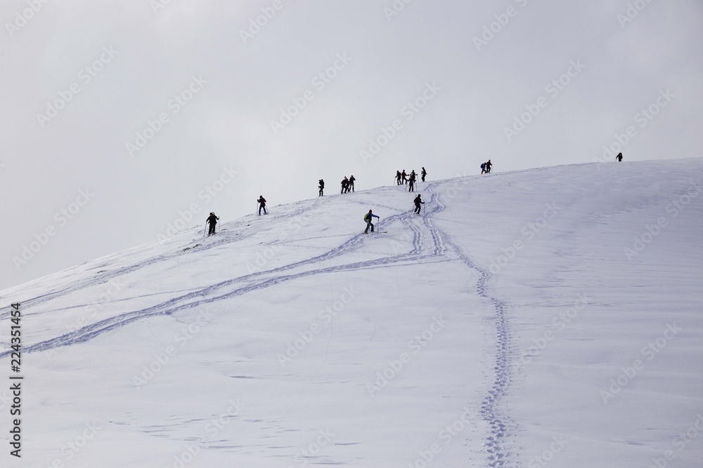 Some hikers face the snowy mountain on a sunny day, equipped with snowshoes.