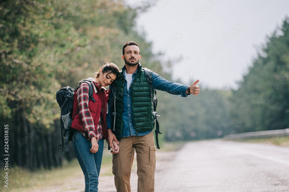couple of travelers with backpacks hitchhiking on road