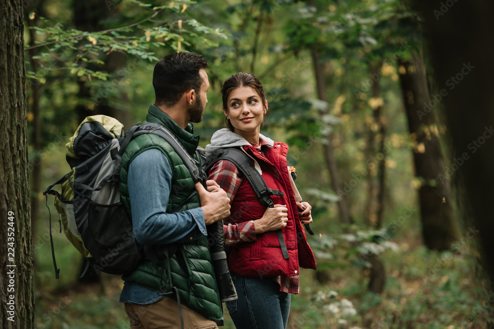 side view of man and woman with backpacks hiking in woods side view of man and woman with backpacks hiking in woods