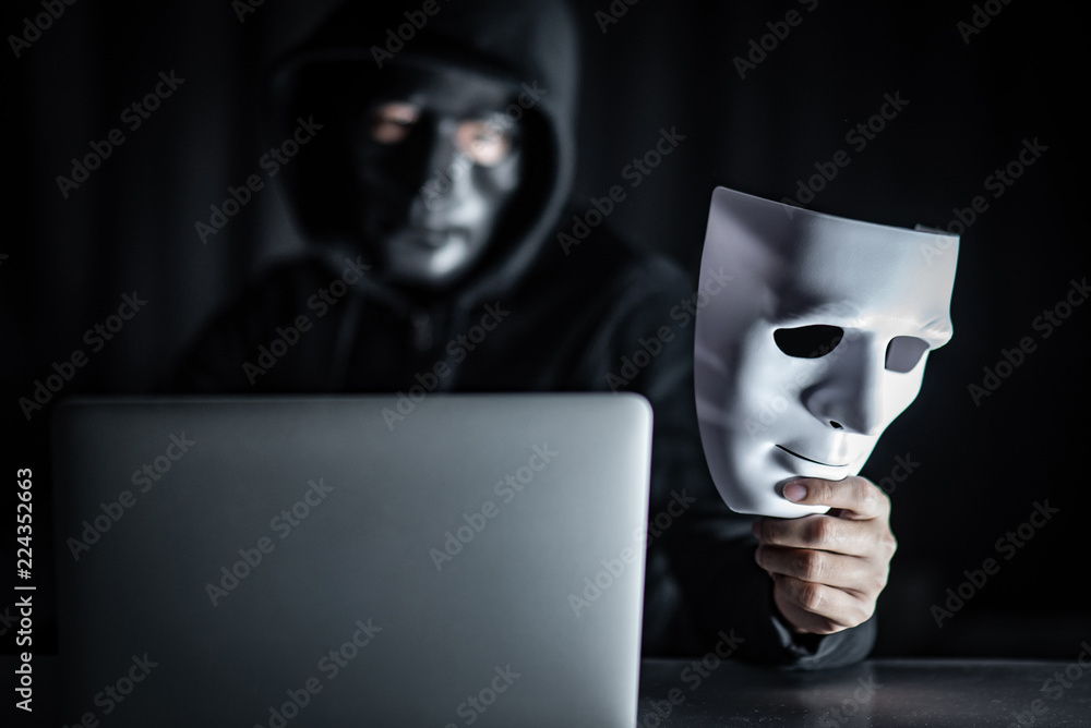 Mystery male hoodie hacker wearing black mask holding white mask with  laptop computer on the table. Anonymous social masking. Ransomware cyber  attack or internet security concepts Stock Photo | Adobe Stock