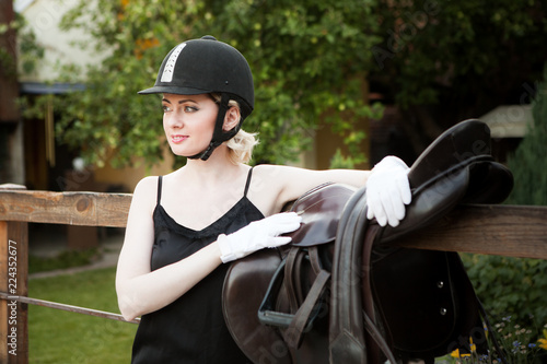 Young beautiful woman in jockey clothes with saddle for riding