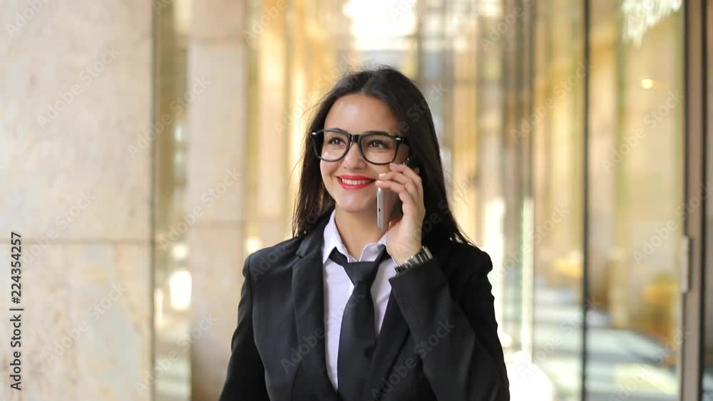 Cute businesswoman walking talking on mobile phone. Steadicam shot, slow motion Cute businesswoman walking talking on mobile phone. Steadicam shot, slow motion