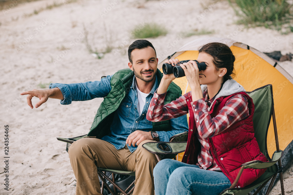 woman looking through binoculars while having camping together with husband on sandy beach