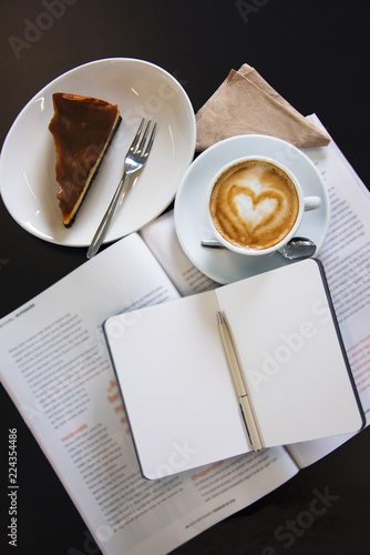 Caramel cheesecake with cappuccino and magazines. Top view shot.