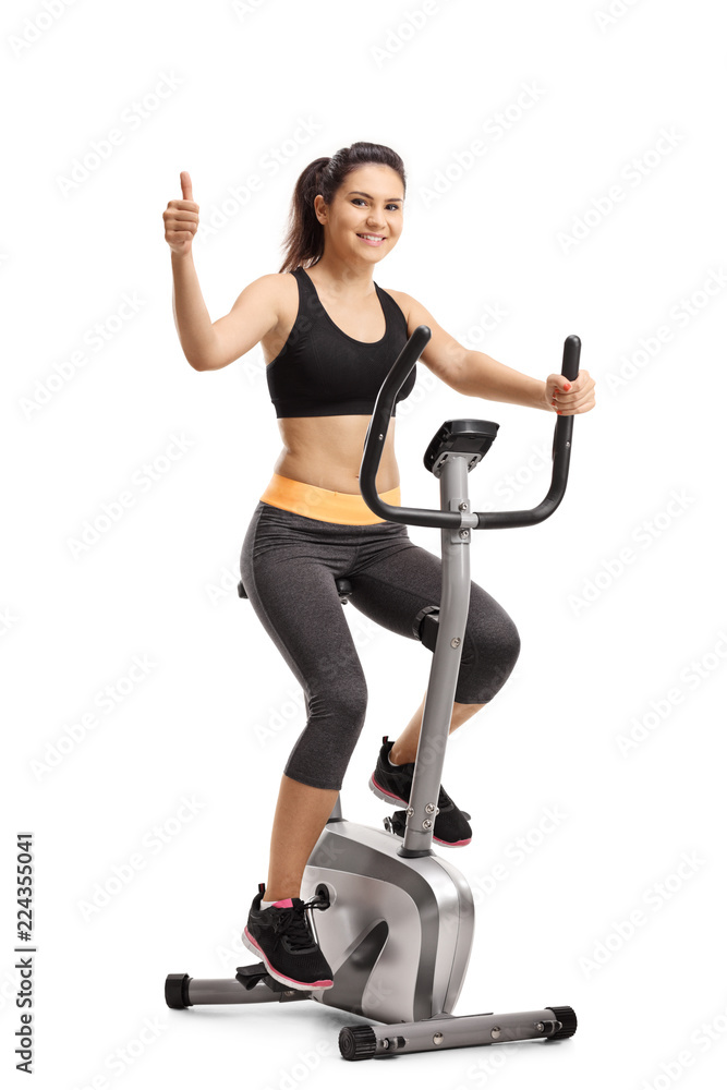 Obraz premium Young female riding a stationary bike and showing thumb up