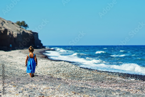 Little girl in a blue dress playing on the Paradisos beach in Santorini photo