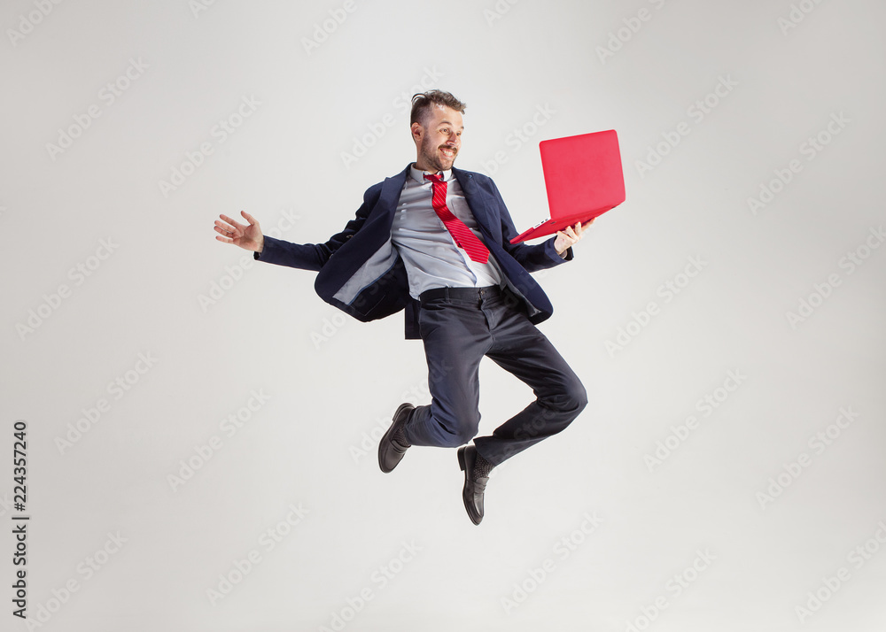 Image of young surprised man over white studio using laptop computer while jumping. illumination in motion