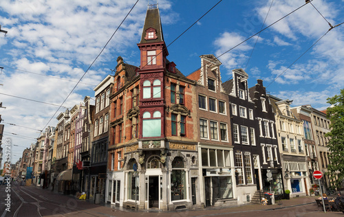 Typical street with old traditional houses in Amsterdam under blue sky.