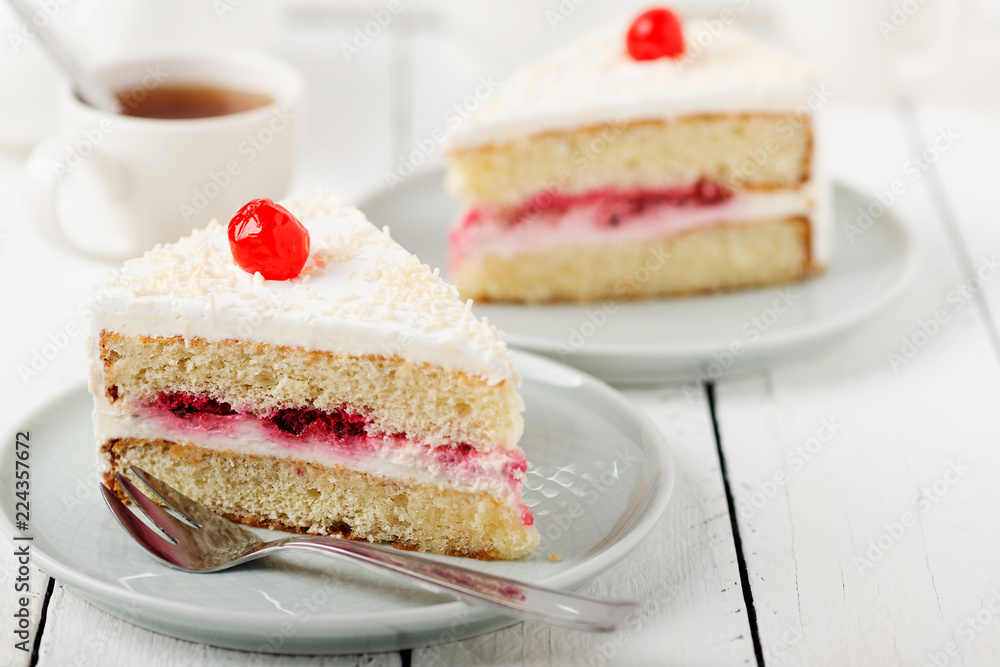 Slice vanilla cake with butter cream icing in the plate on white wooden table.