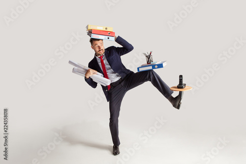 Young businessman in a suit juggling with office supplies in his office, isolated on white background. Conceptual collage with phone, folders. The business, office, work concept.