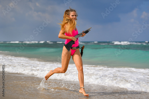 Beautiful sexy girl in a swimsuit with a carbine runs along the seashore