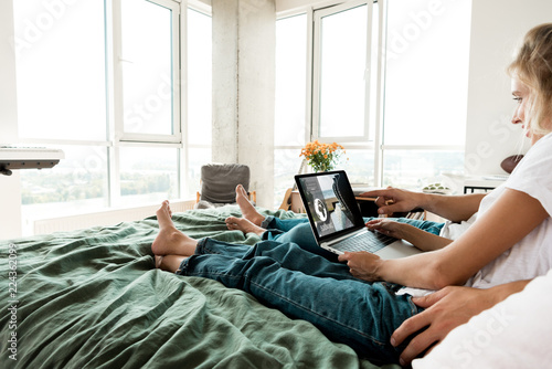 partial view of couple with digital laptop with booking lettering on screen resting on bed at home